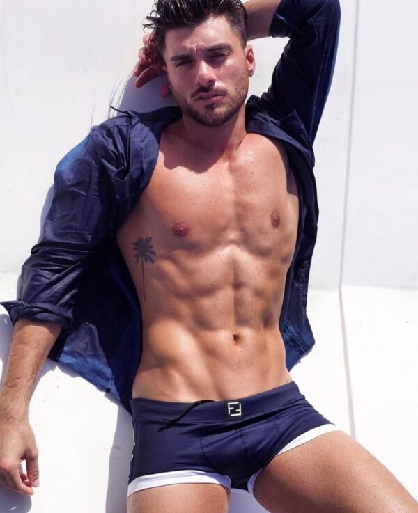 Shirtless man posing in swimwear outdoors.